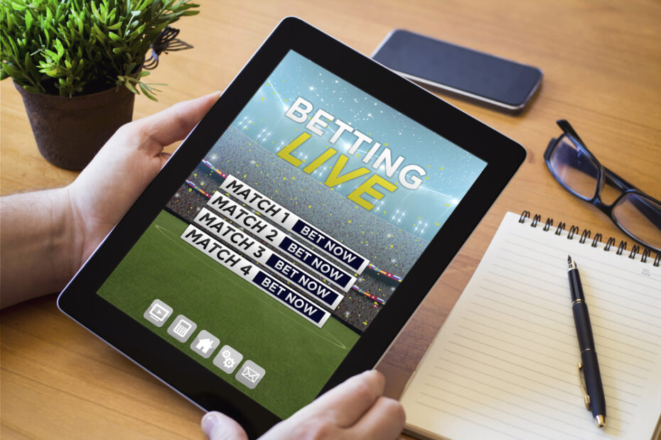 hands of a man holding a online betting device over a wooden workspace table. All screen graphics are made up.